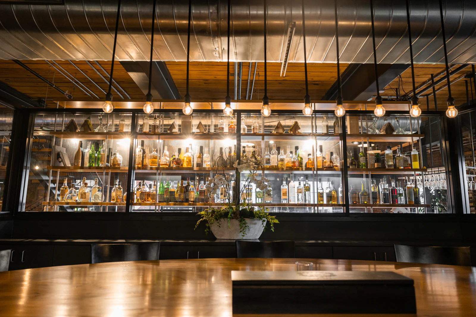A hospitality bar with lit back shelving and pendant lights over a timber counter.