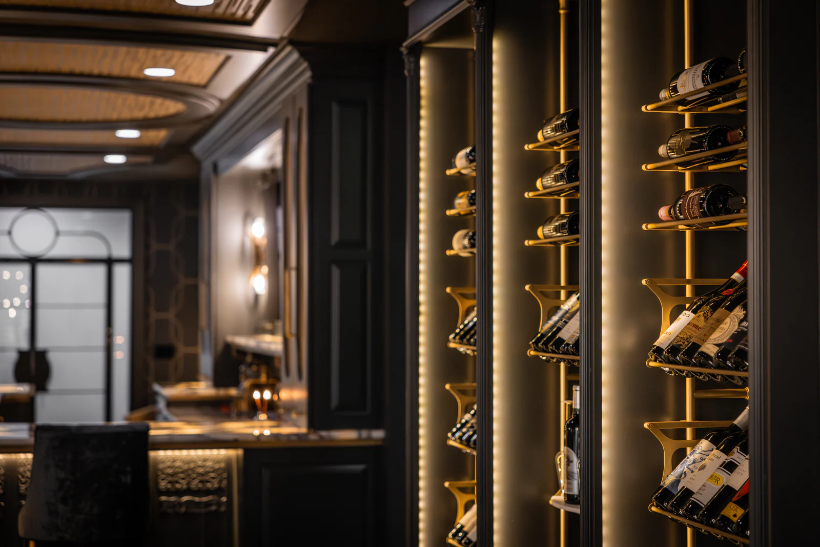 Brass bottle supports and vertical light channels set into dark cabinetry.