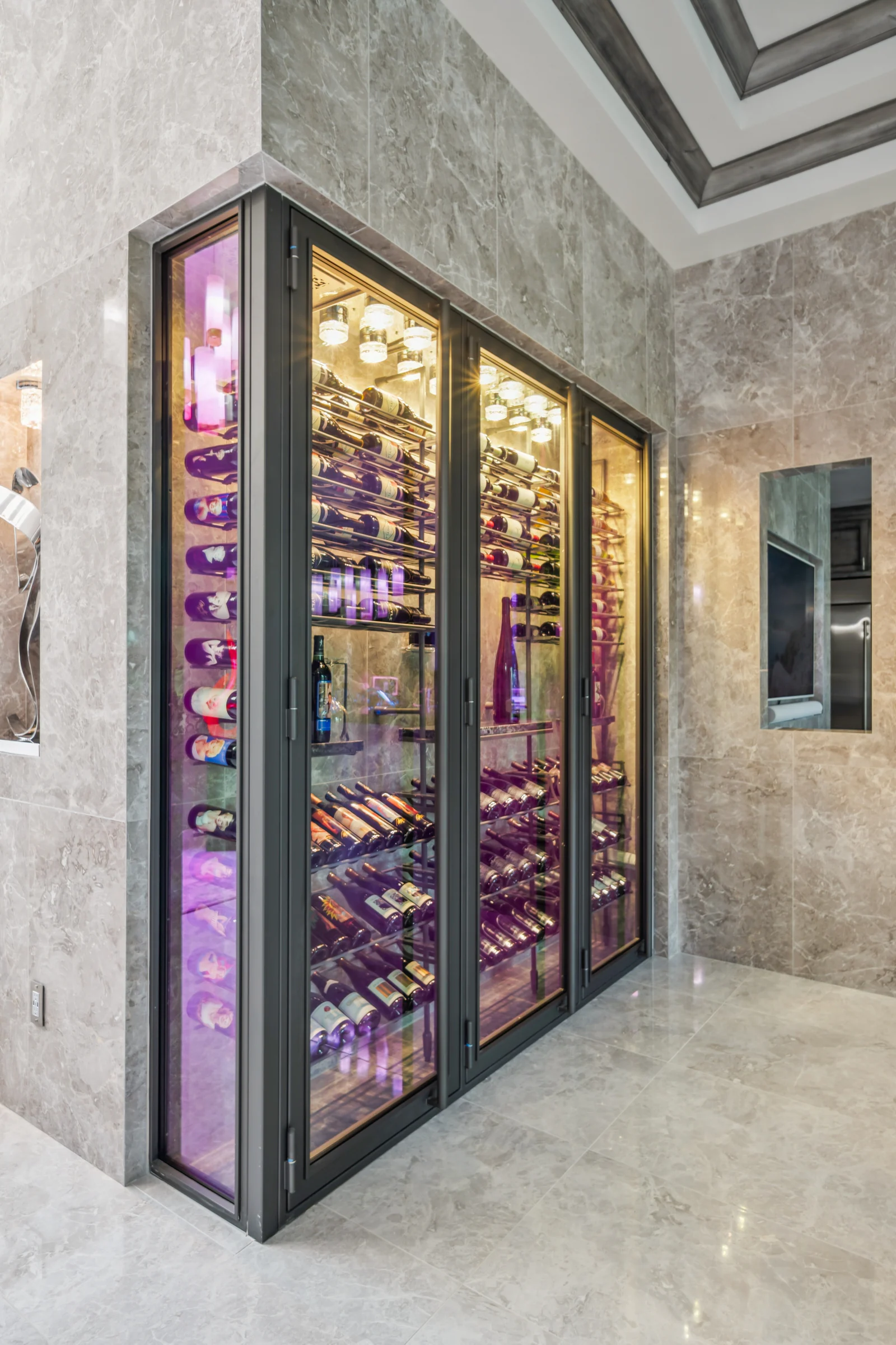 A tall glass wine cabinet built into pale stone walls.