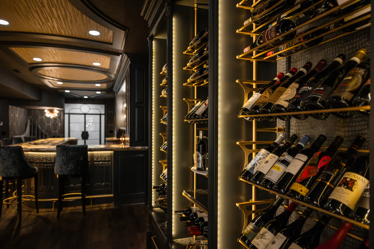 A bar and lounge seen past brass wine racks lit in vertical channels.
