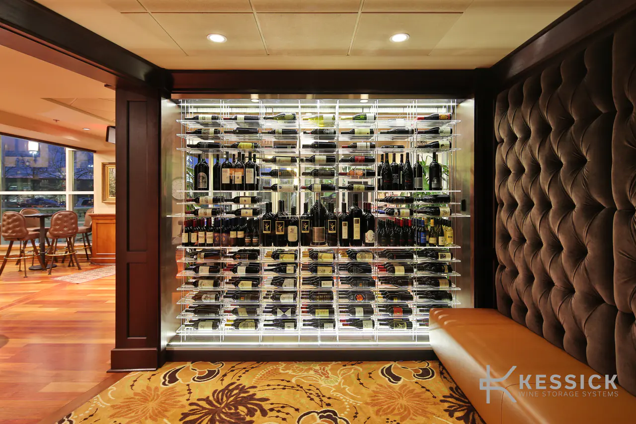 A glass-fronted wine wall lit from within, beside a tufted velvet wall and a leather banquette.