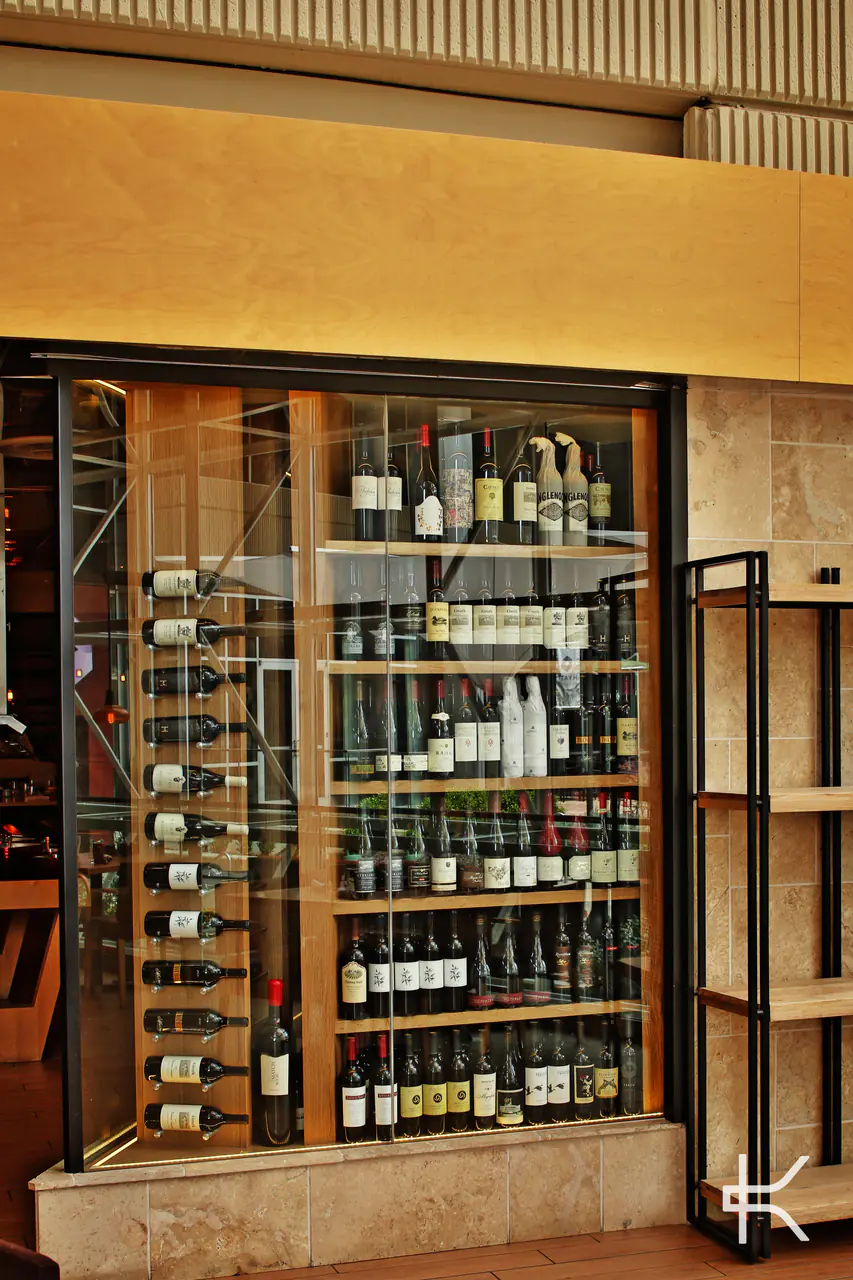 Timber shelves of wine behind a black steel and glass front.