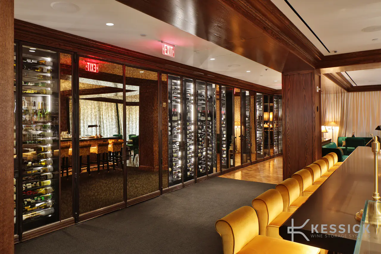 A long glass wall of wine beside a bar lined with gold stools.