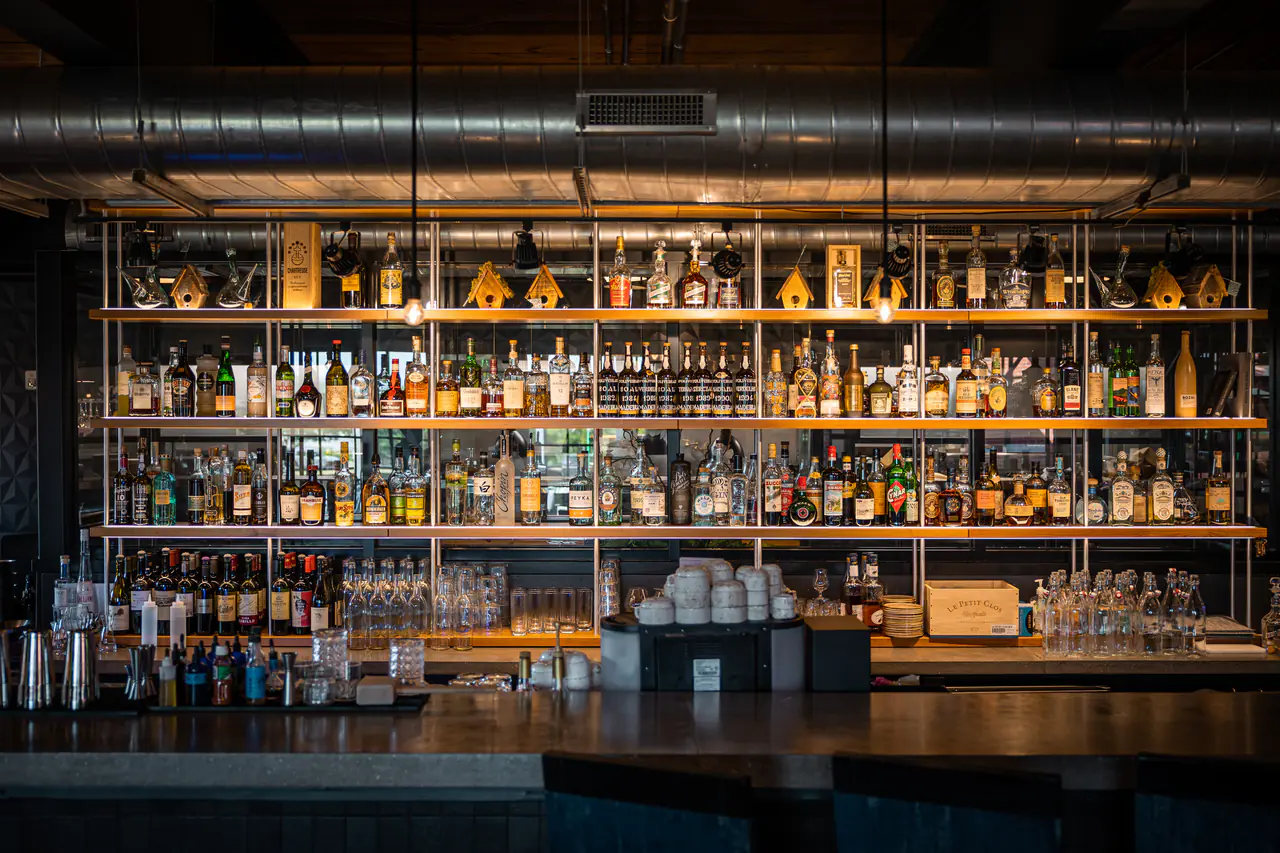 An open back bar of spirits on timber shelves, seen straight on across the bar.