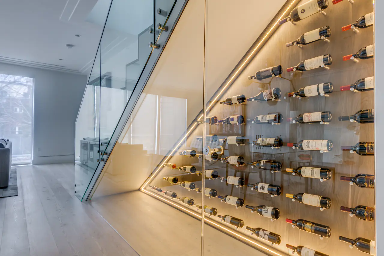Bottles held on pegs along a lit wall beneath a glass-sided staircase.