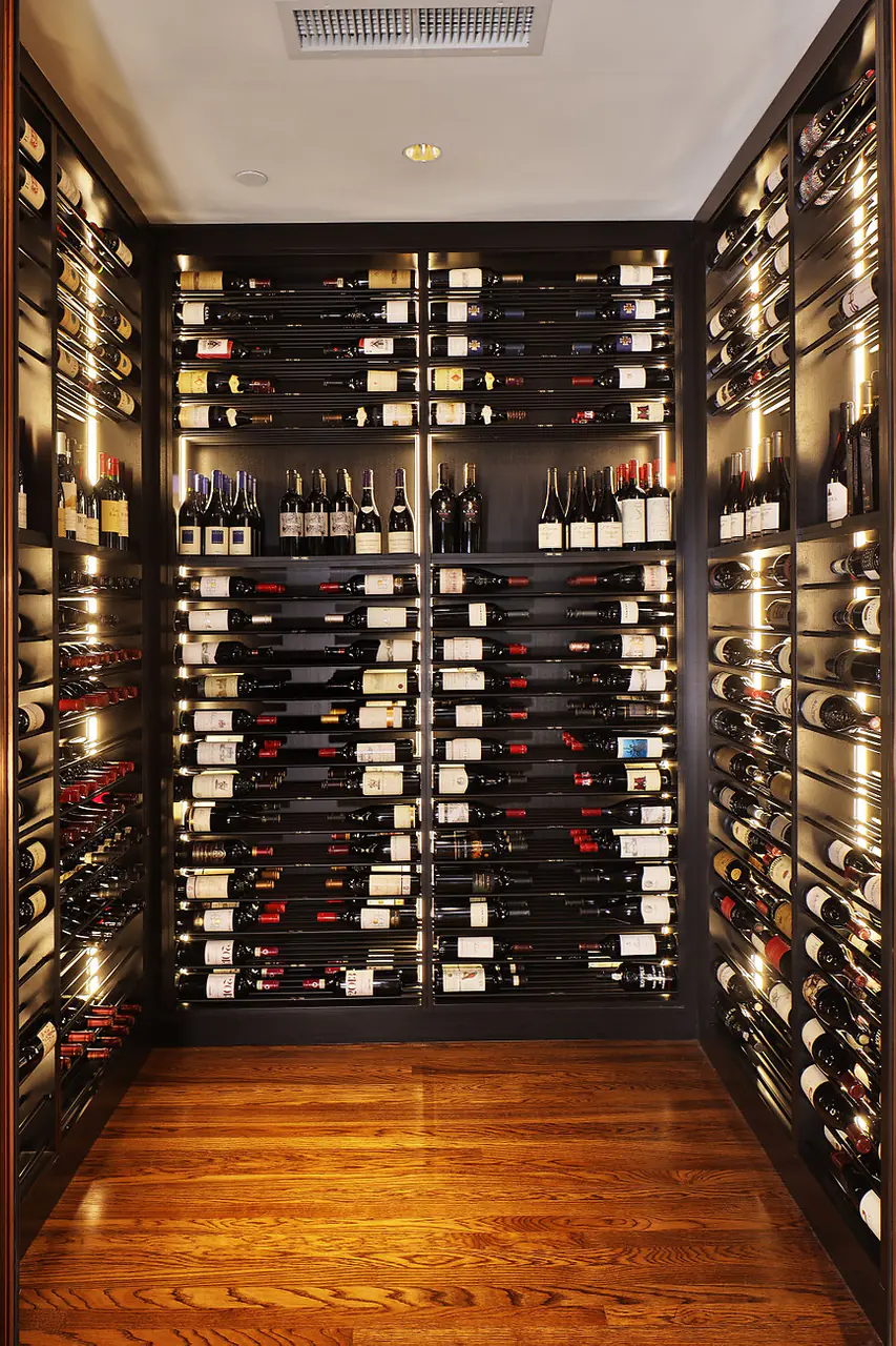 The end wall of a narrow wine room, dark racks lit floor to ceiling.