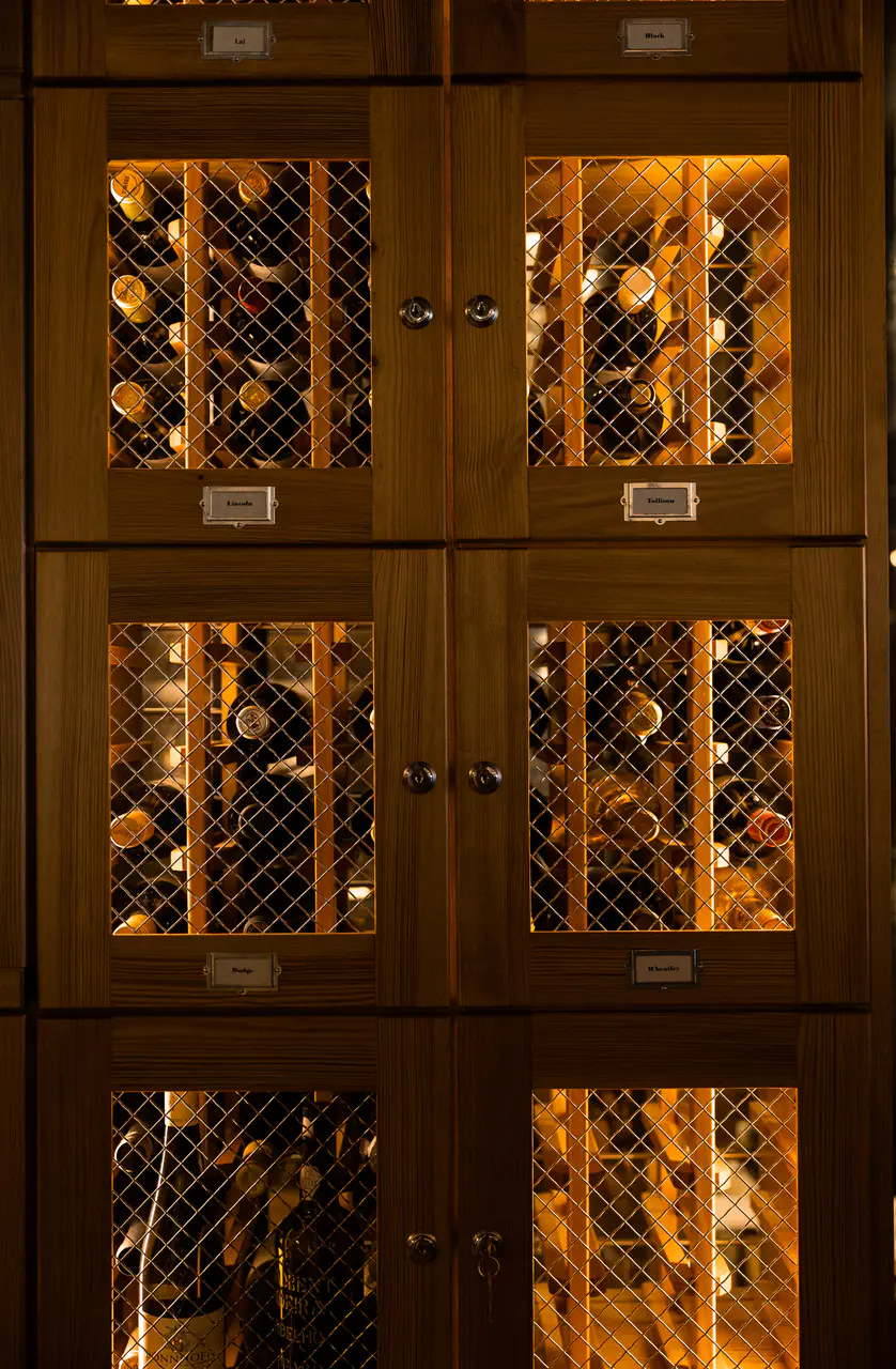 Timber locker doors with lattice fronts, bottles lit inside.