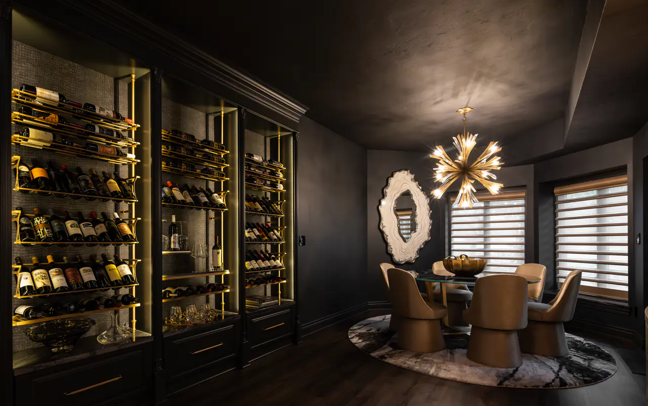 A dark dining room lined with lit brass wine racks, a starburst chandelier over a round table.