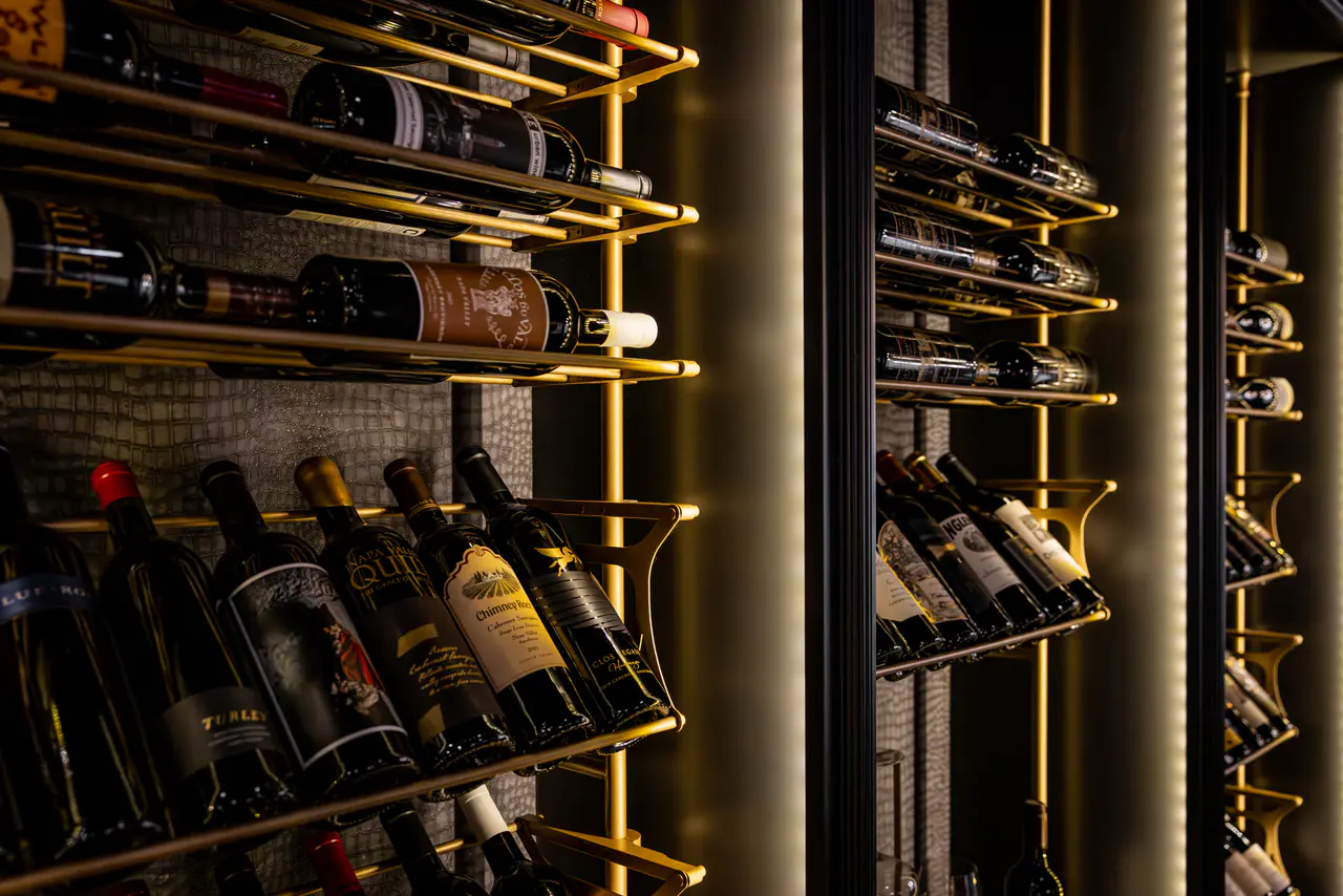 Bottles in brass cradles, lit from behind in a dark cabinet.