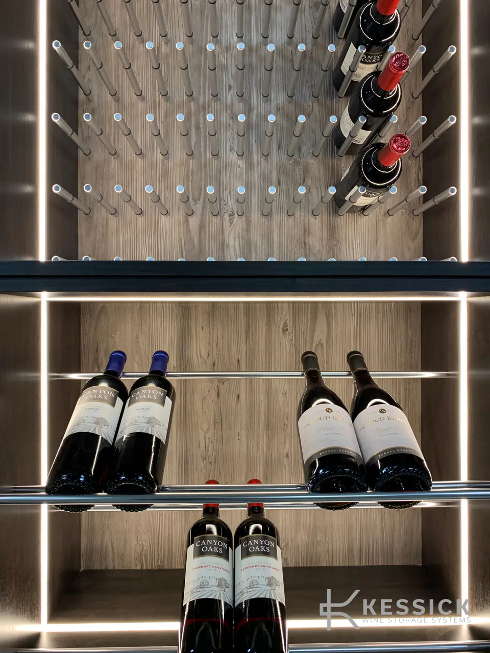 Wine bottles on polished steel pegs between lit shelves.