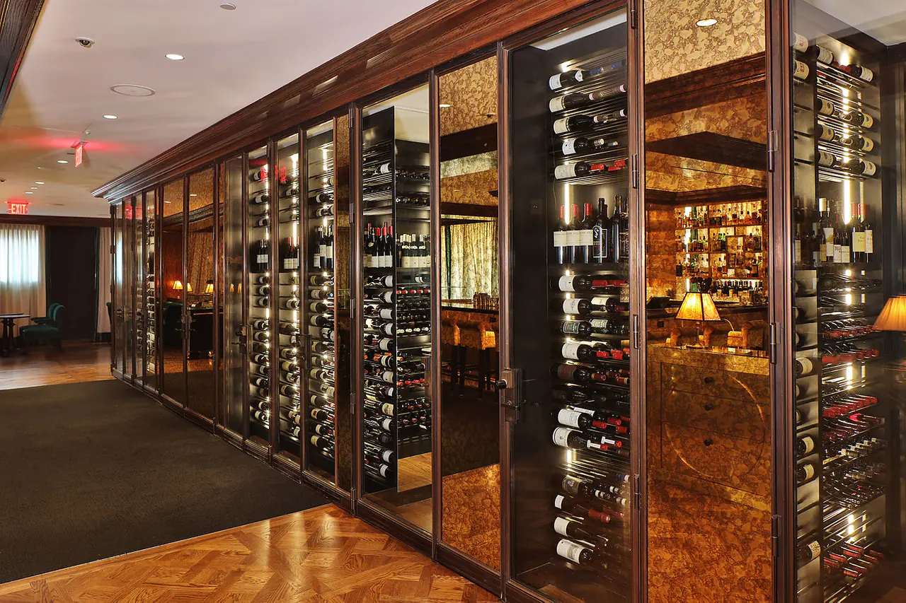 Glass walls of wine around a lounge, a bar lit beyond.
