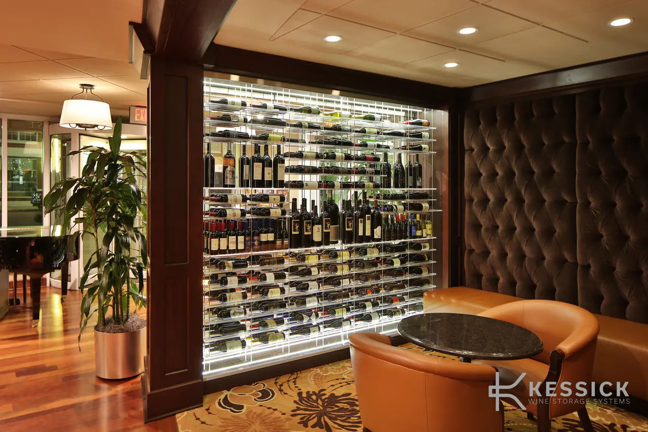 A glass-fronted wine wall in a lounge, between a tufted wall and a grand piano.