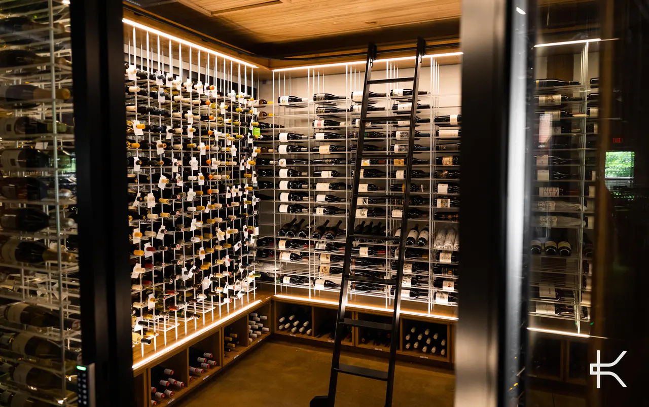 A wine room seen through its open glass door, racks lit on three walls.