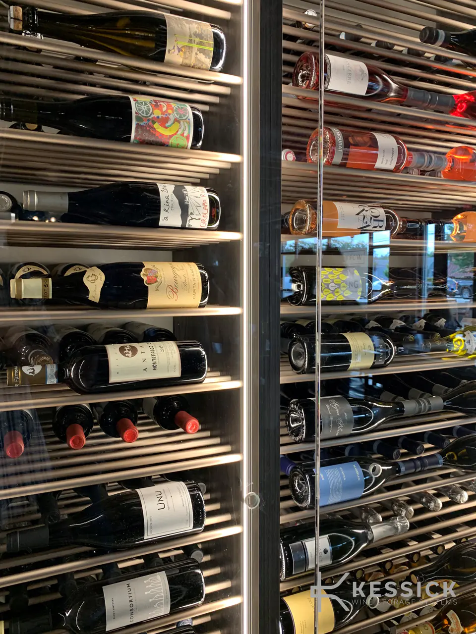 Bottles on polished steel rods behind a glass door, close up.