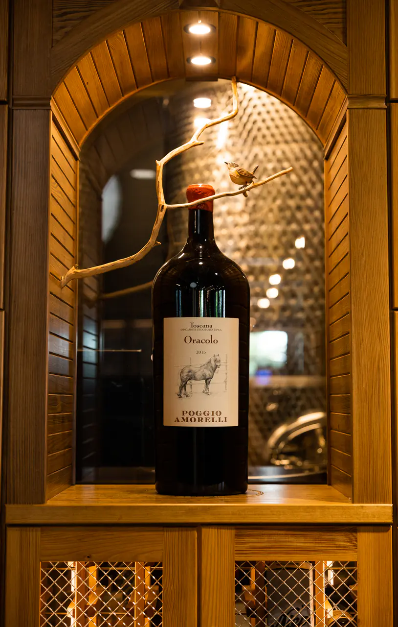A large-format bottle in an arched timber niche, a branch with a small bird above it.
