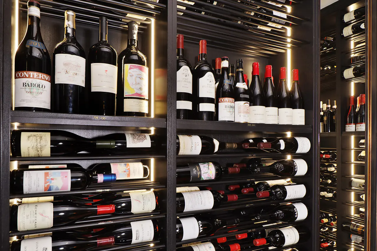 Large bottles standing above rows of wine on dark rods.