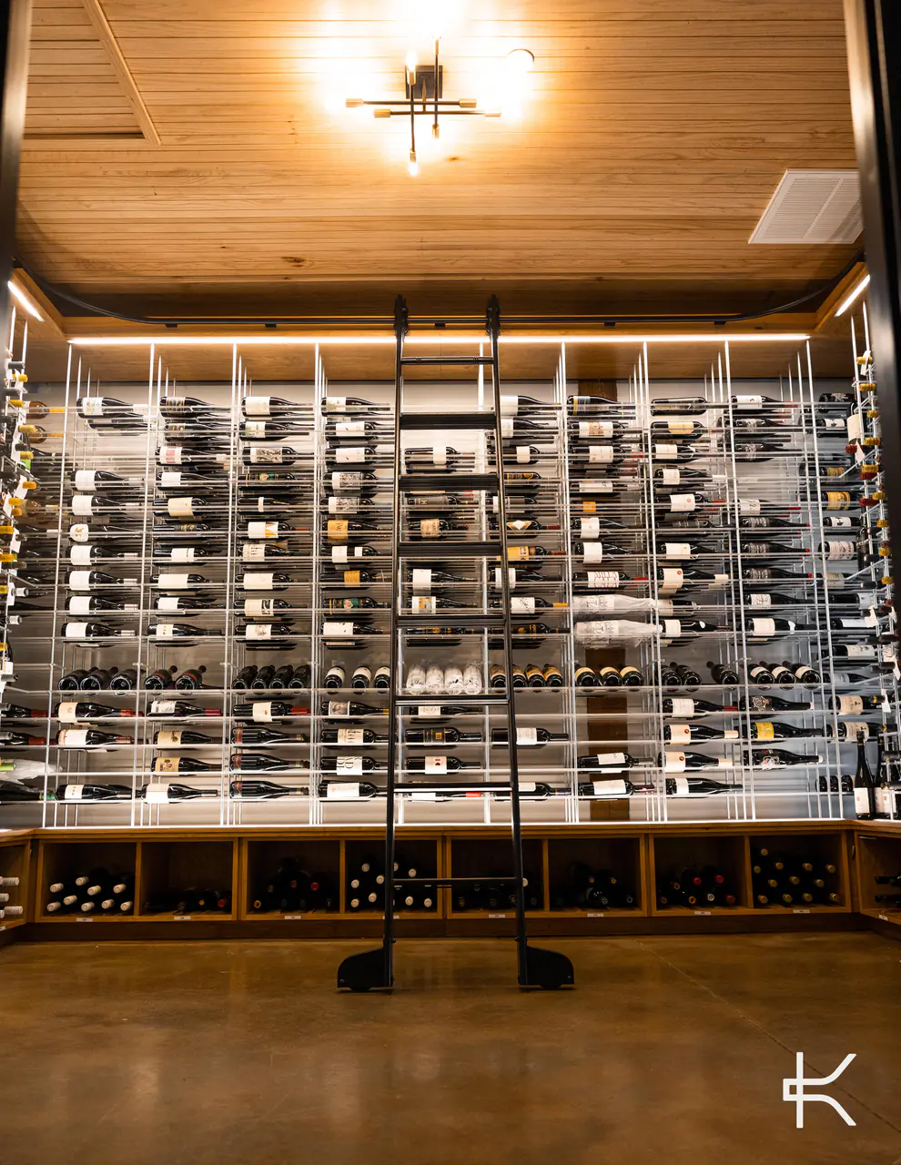 A wine room lined floor to ceiling with white steel racks, a library ladder on its rail.