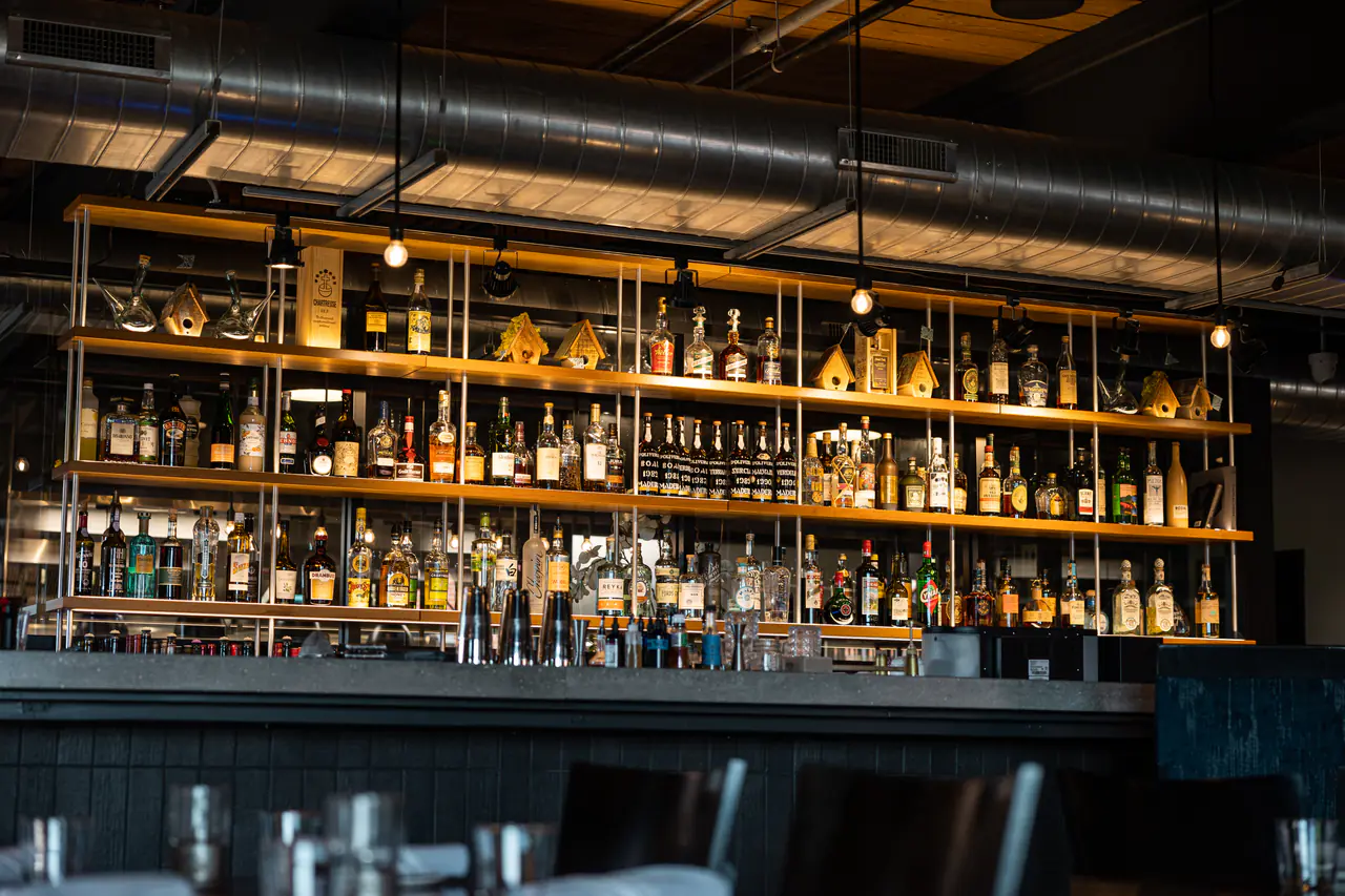 An open back bar of timber shelves on a white steel frame, lined with spirits.