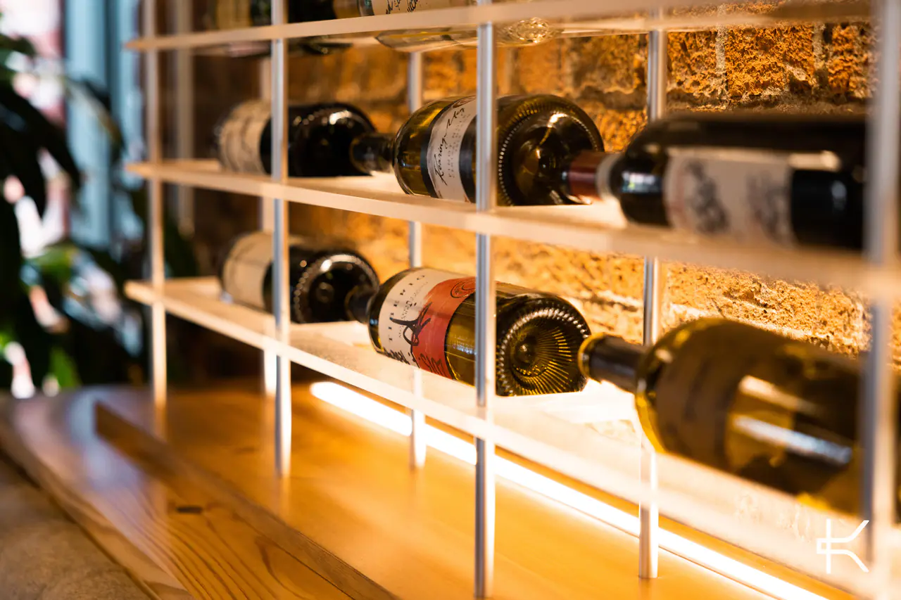 Bottles held by a white steel frame against stone, a light strip along the timber base.