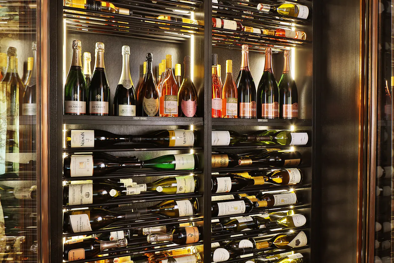 Champagne and rosé on a dark shelf, bottles on rods below.