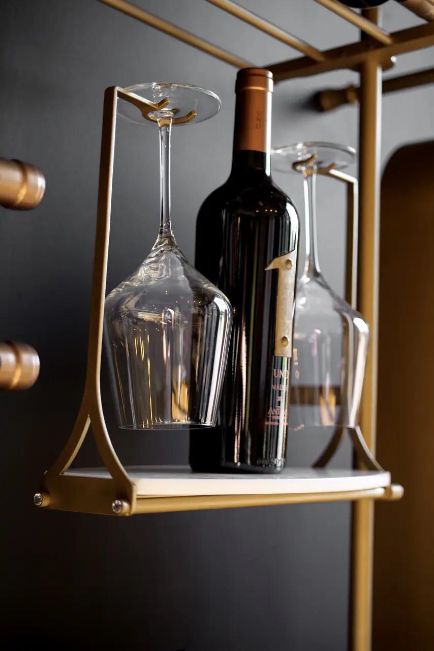 A bottle and two glasses on a brass-framed shelf, close up.