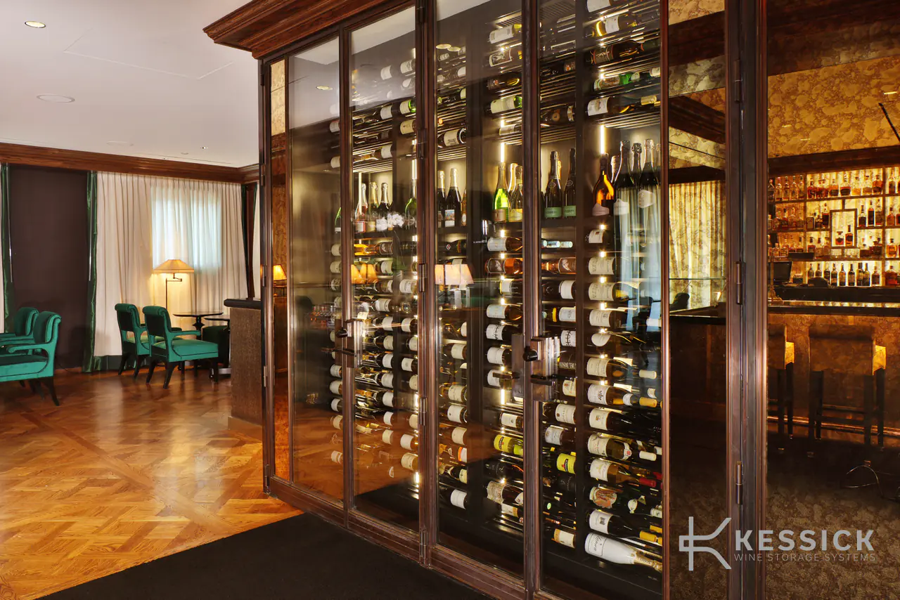 A glass-walled wine room along a lounge, a bar glowing through the glass.