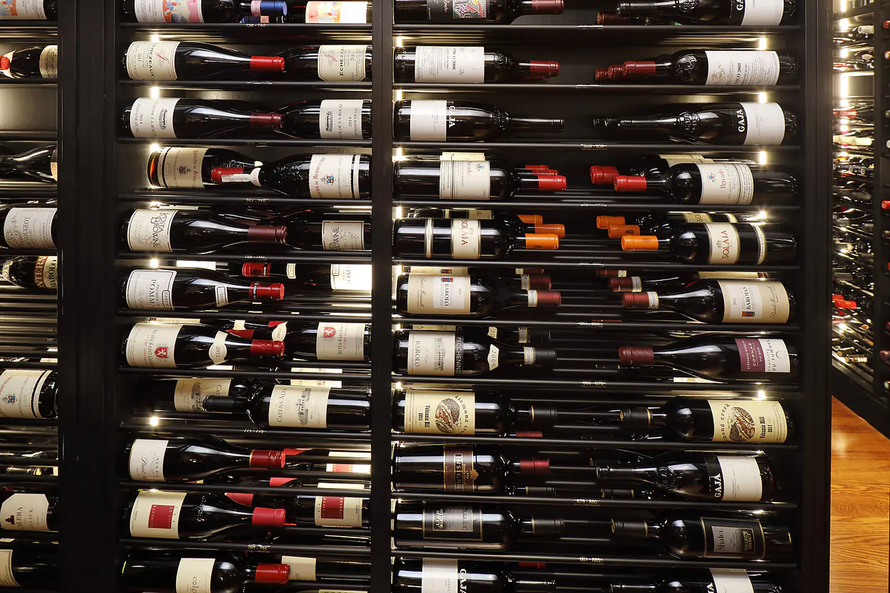 A dark rack wall of wine laid on slim rods, labels forward.