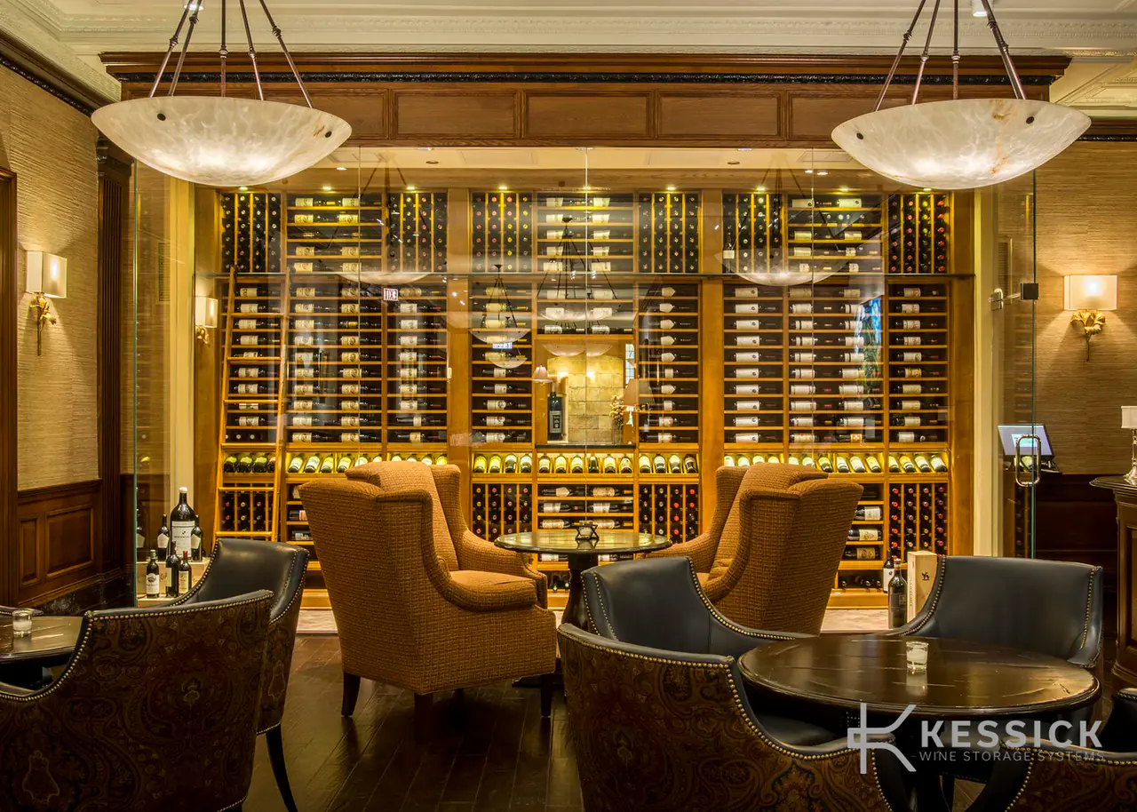 A lounge of leather armchairs before a glass-fronted wine room, alabaster pendants above.