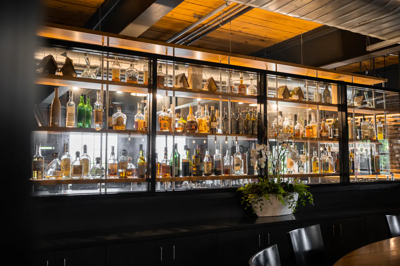 A glass-fronted back bar of spirits seen at an angle, an orchid on the counter.