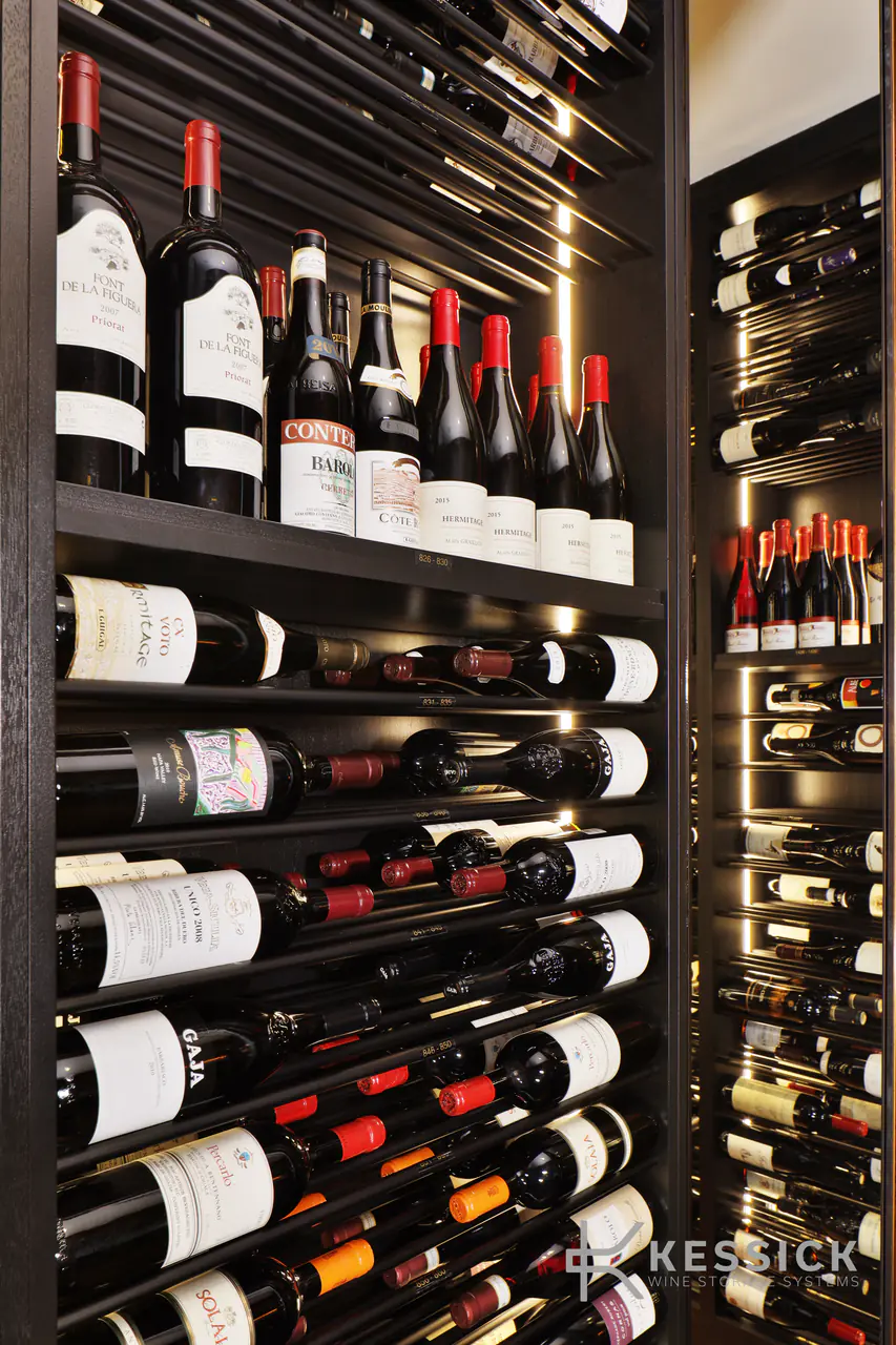 Large-format bottles above rows of wine on dark rods, lit from the side.