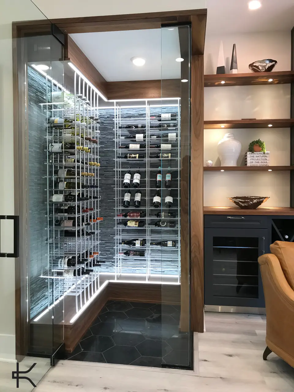 A glass-fronted wine room beside built-in shelves and a leather armchair.