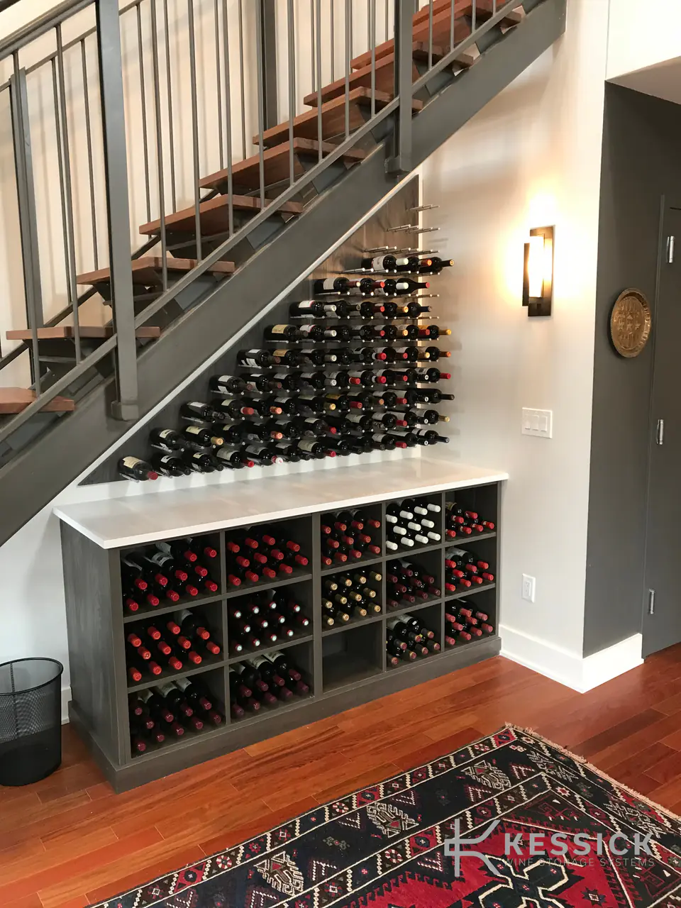 A wine wall beneath a staircase, above a cabinet of cubbies.