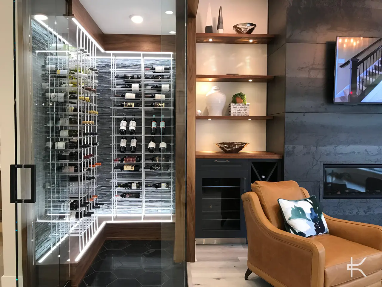 A glass wine room off a living room, white racks against a stone wall, a leather armchair beside it.