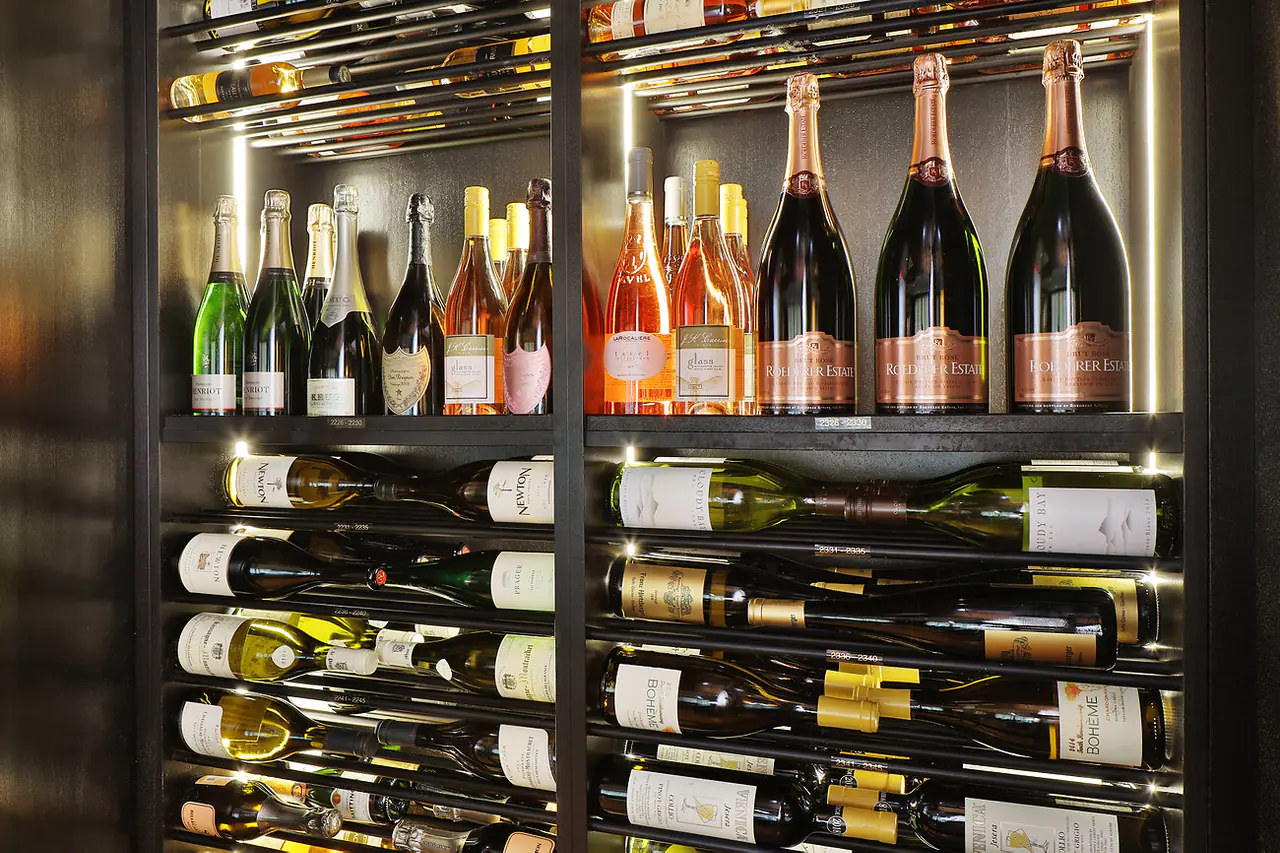 Magnums of champagne and rosé above rows of white wine on dark rods.
