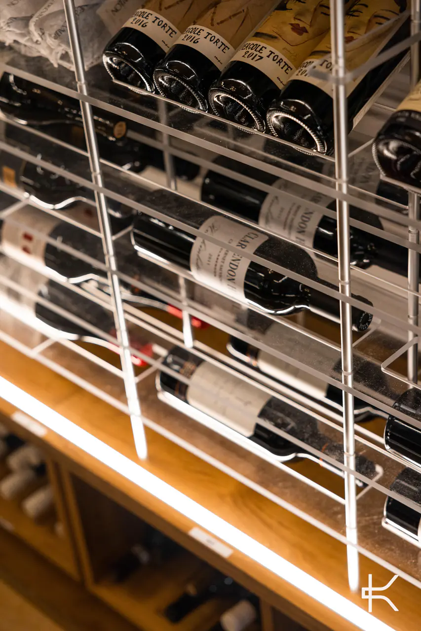 Bottles lying in white steel racks above a lit timber base.