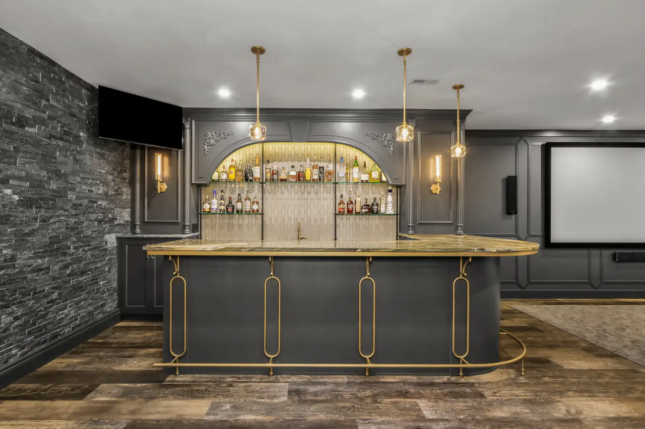 A curved bar on brass supports with a foot rail, a lit arched back bar and a stacked-stone wall beside it.