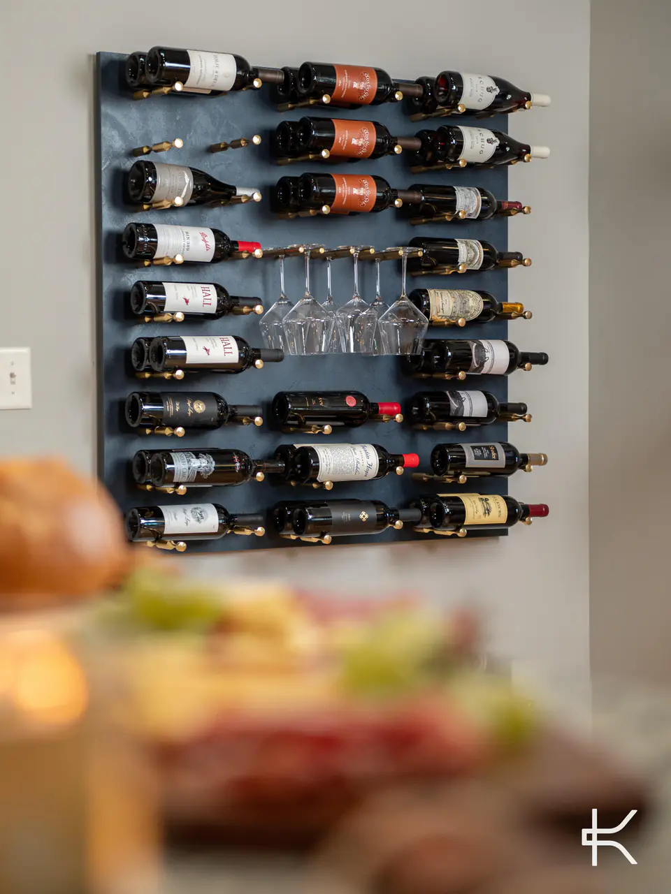 A wall panel of wine and hanging glasses behind a table set with food.