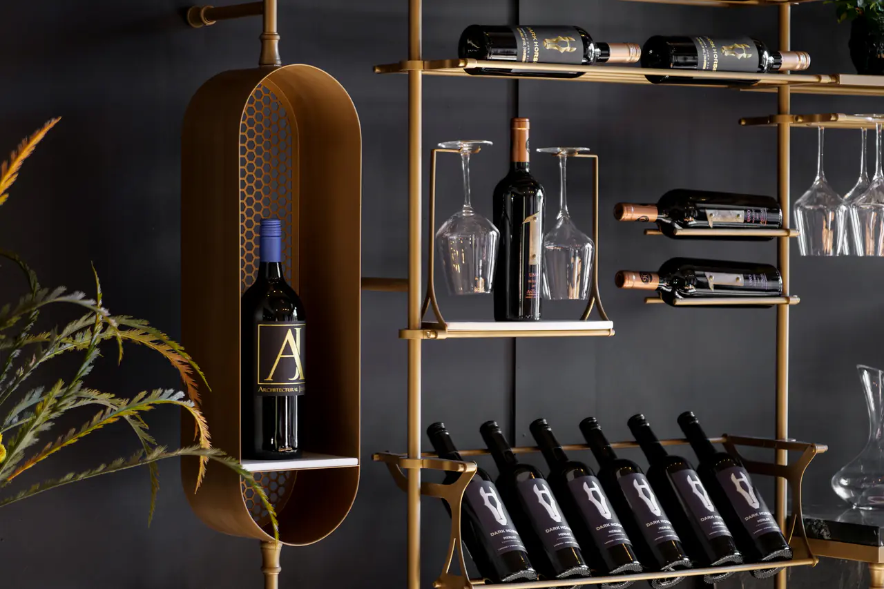A brass wine wall on black panelling, a capsule niche, a glass shelf with glasses and bottles on pegs.
