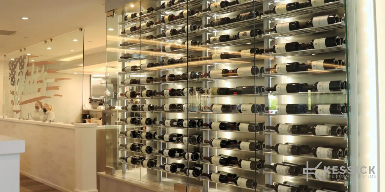 A glass wall of wine on steel rods beside a bright counter.