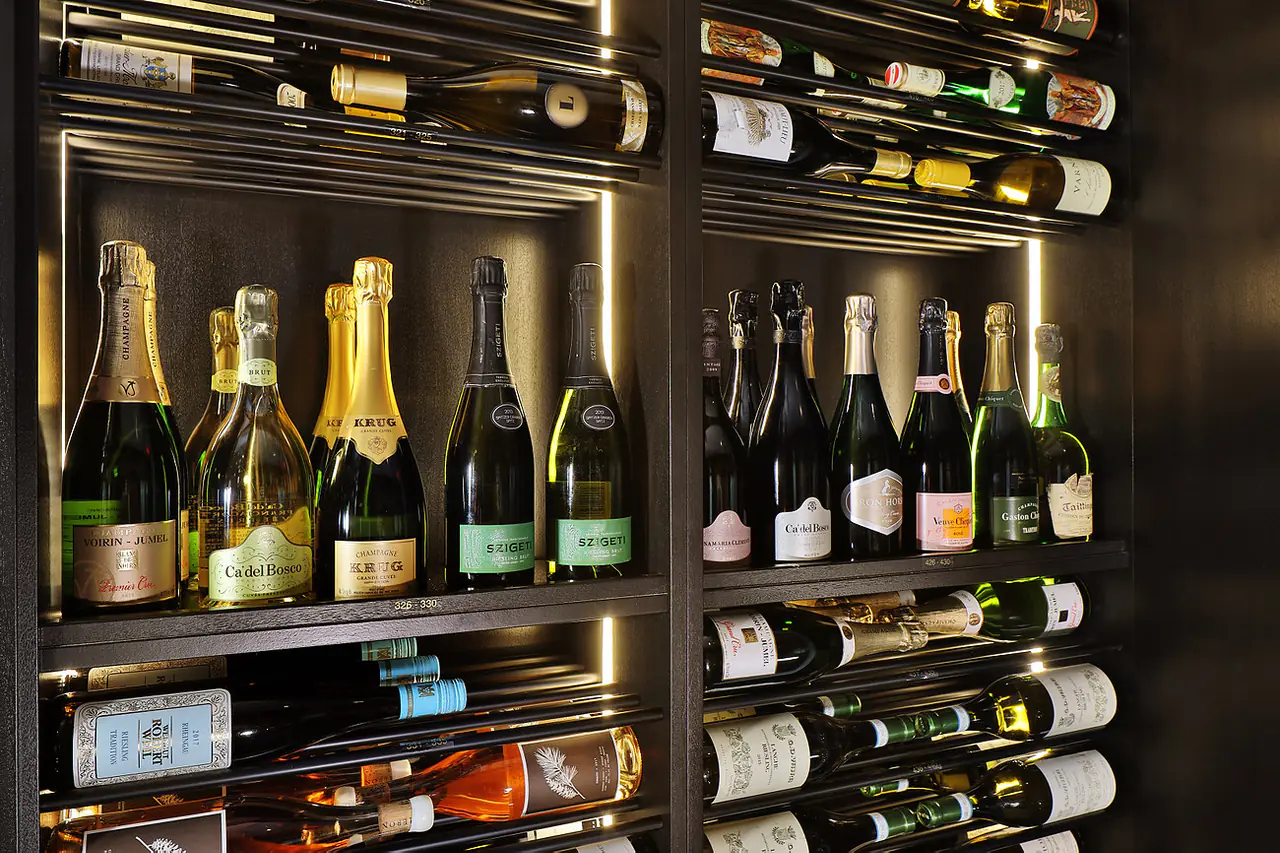 Champagne standing on dark shelves above bottles on rods.