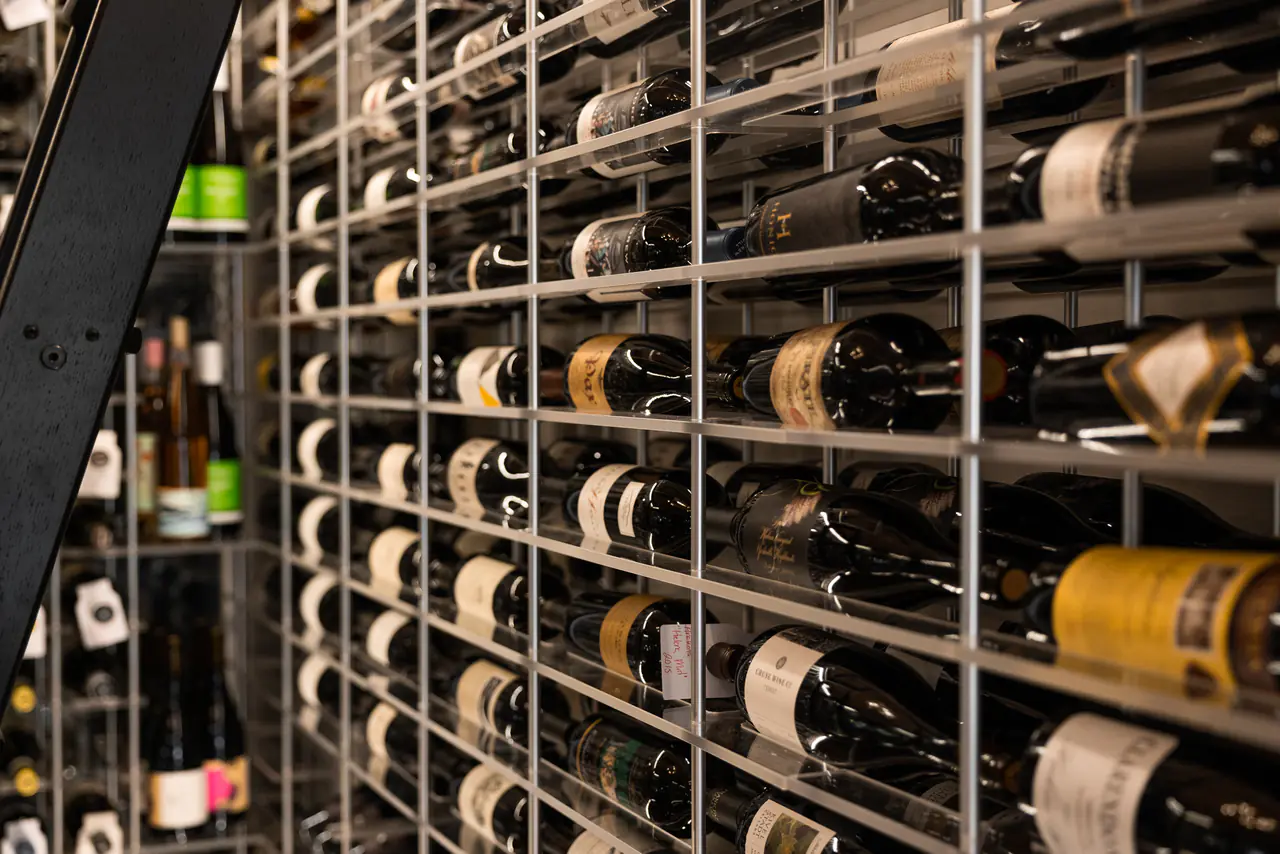 Bottles resting on white steel rods, the edge of a ladder at left.