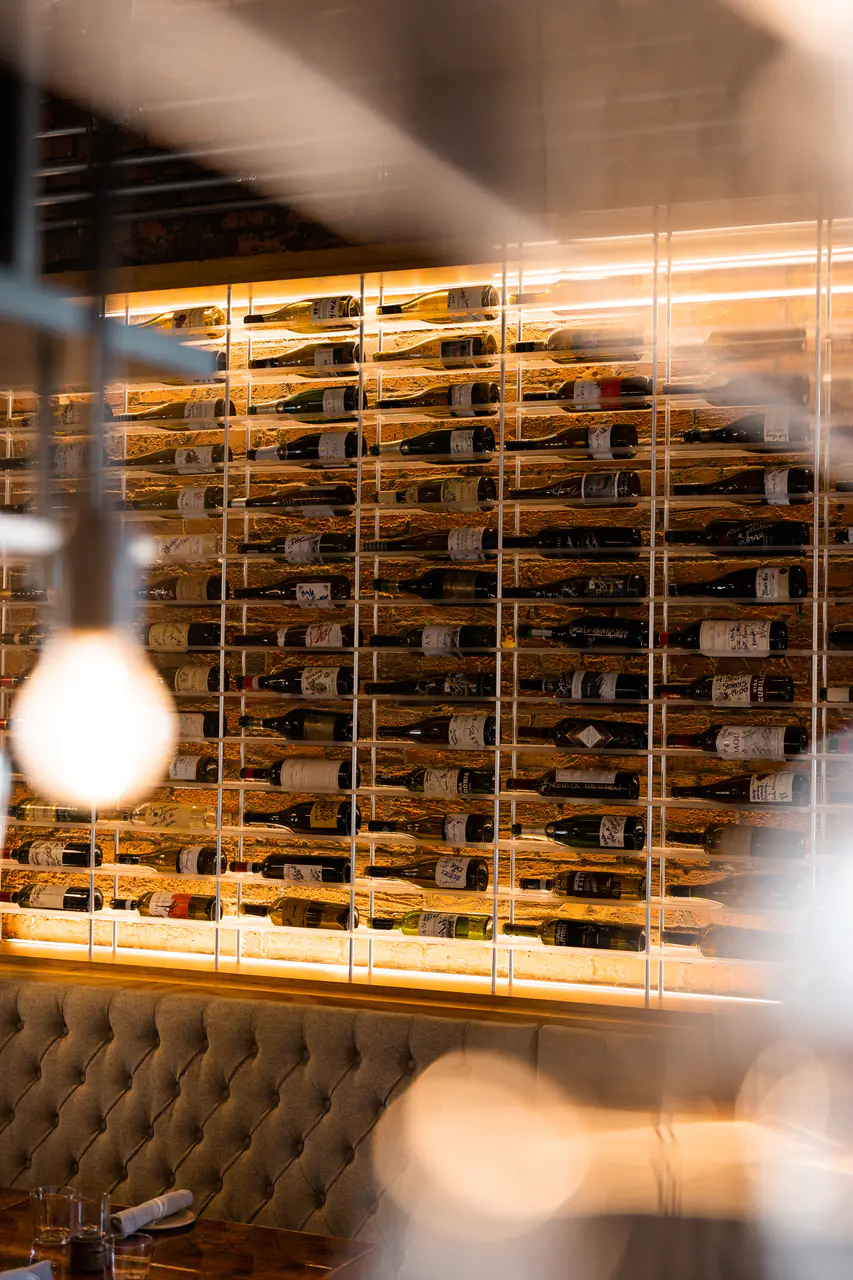 A wine wall above a tufted banquette, a bare bulb in the foreground.