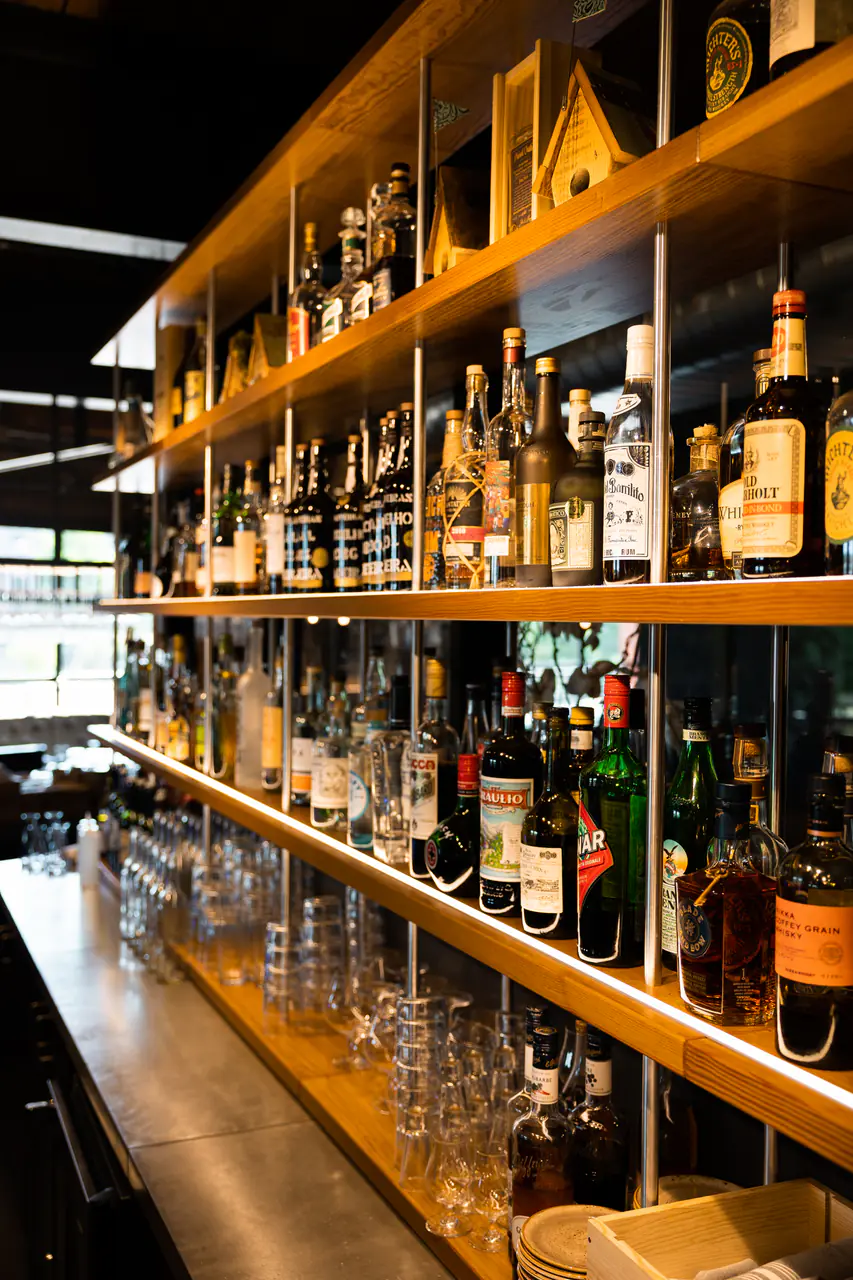 Open shelves of spirits and glassware above a steel bar counter.