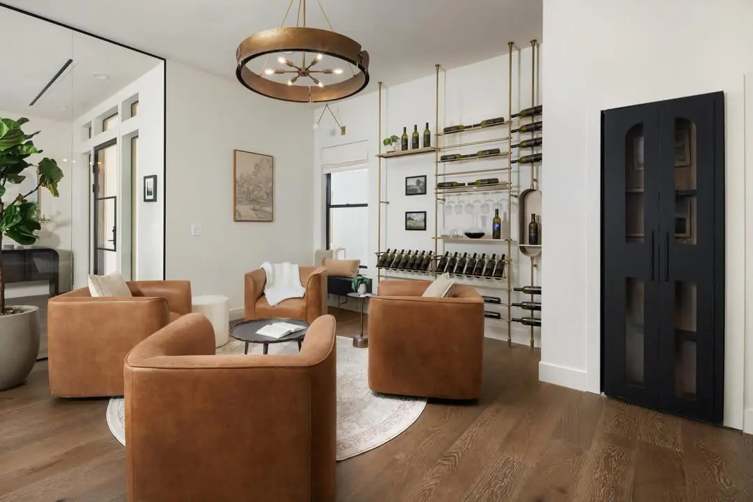 Leather armchairs around a round rug, a wall of slim metal wine shelves behind them and a black double door.