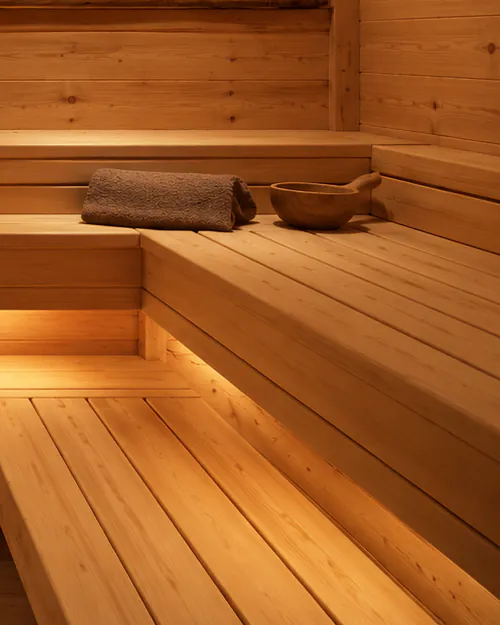 The corner of two timber benches meeting in an L, warm light running beneath the upper one.